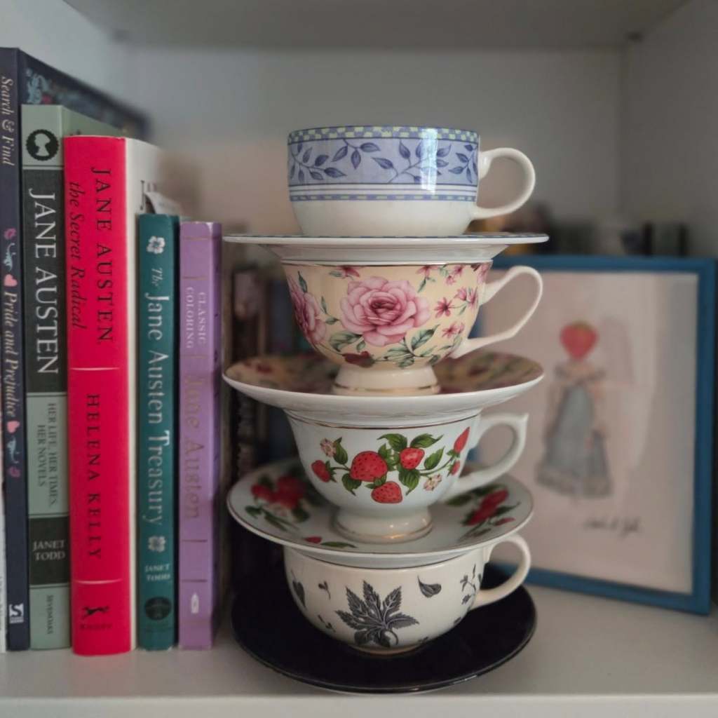 a stack of four floral china tea cups next to some Austen-related books
